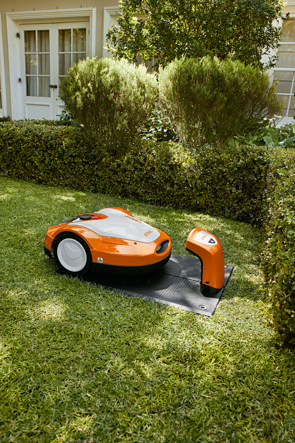 Το χλοοκοπτικό ρομπότ STIHL iMOW® RMI 632 είναι σταματημένο δίπλα στη βάση φόρτισης σε έναν κήπο